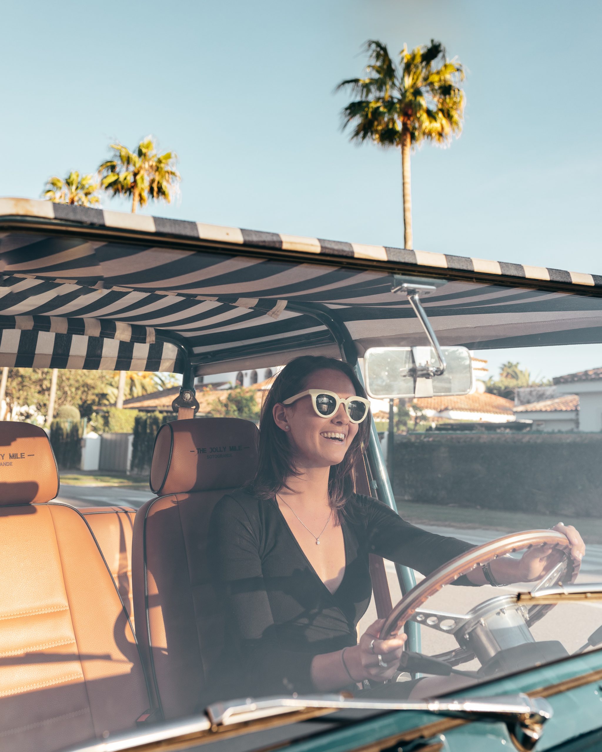 Young lady smiling as she drives a Moke down the road on a sunny day.