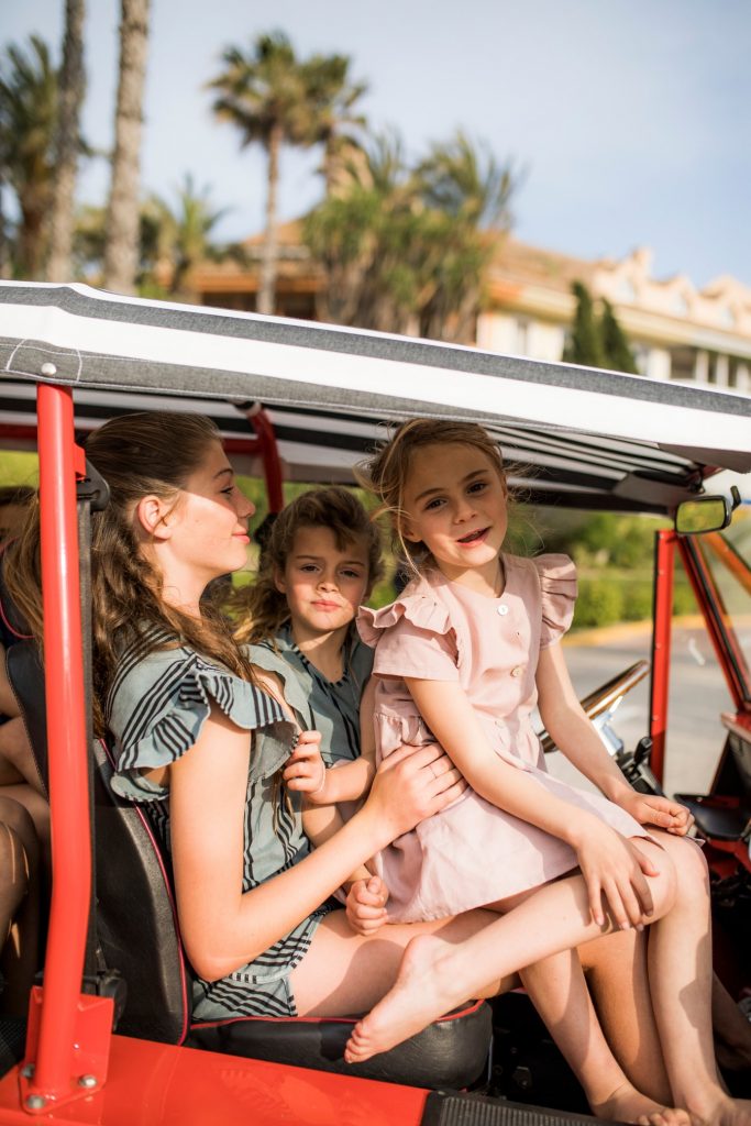 Mother with her two young daughters sitting in a Moke vehicle on a sunny day.